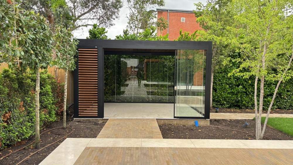 Glass sided aluminium outdoor room installed in a mature garden