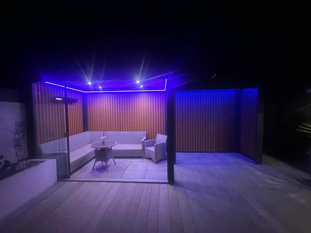 LED lighting glowing under an aluminium pergola roof on a garden terrace at night